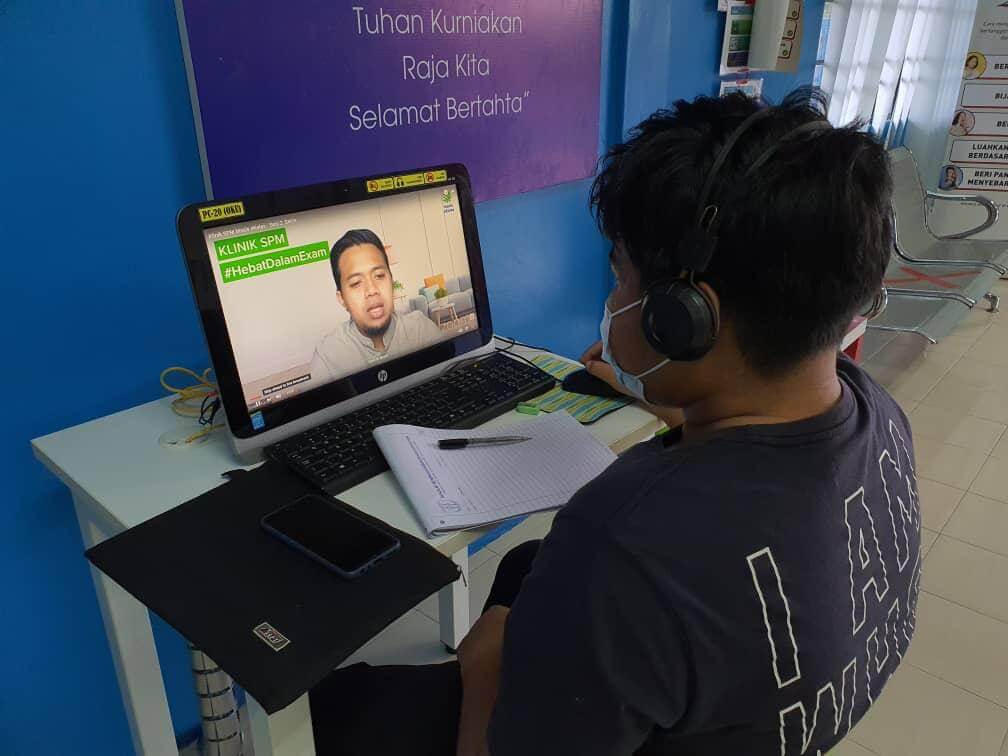 A student using the computer at Pusat Internet and getting exam tips from eKelas teacher during the clinic